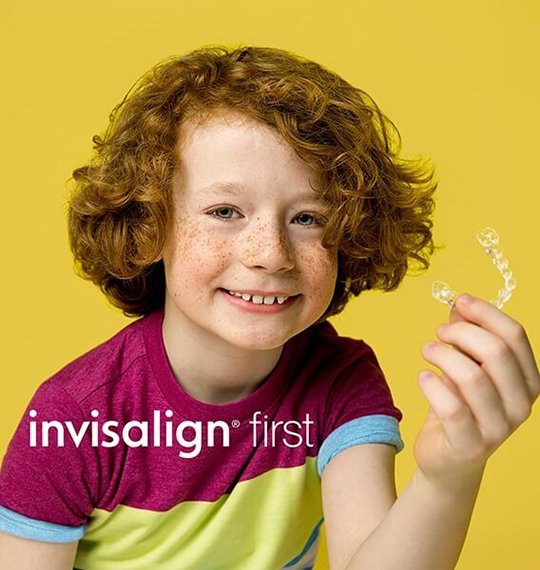 A child holding an Invisalign First clear aligner &mdash; manufacturer photograph, not taken at the clinic